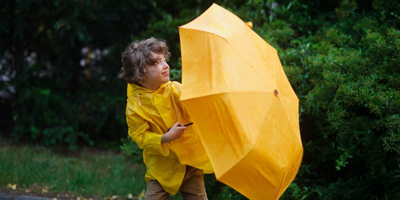Wie entsteht eigentlich Wind? Kind mit Regenschirm im Wind